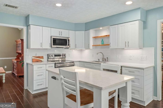 kitchen featuring a textured ceiling, stainless steel appliances, sink, a center island, and white cabinetry