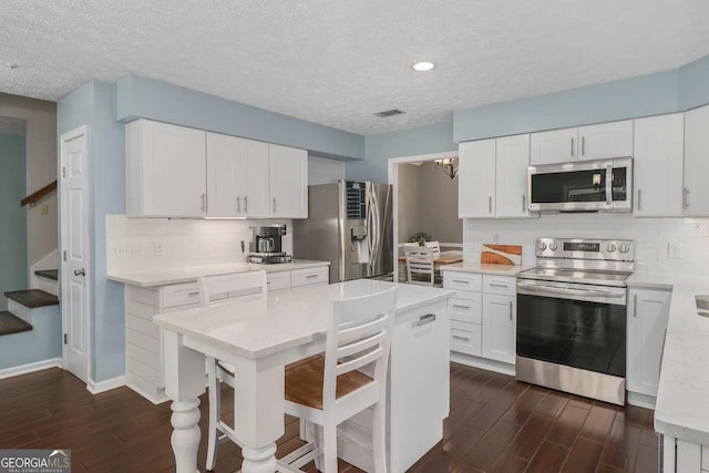 kitchen with light stone countertops, stainless steel appliances, tasteful backsplash, a textured ceiling, and white cabinets