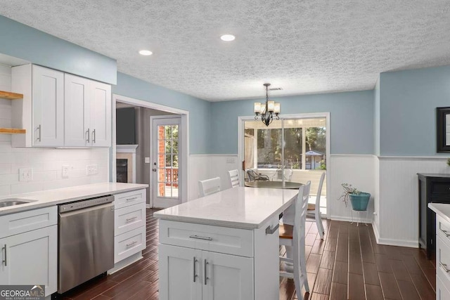 kitchen featuring stainless steel dishwasher, a breakfast bar, a textured ceiling, white cabinets, and hanging light fixtures