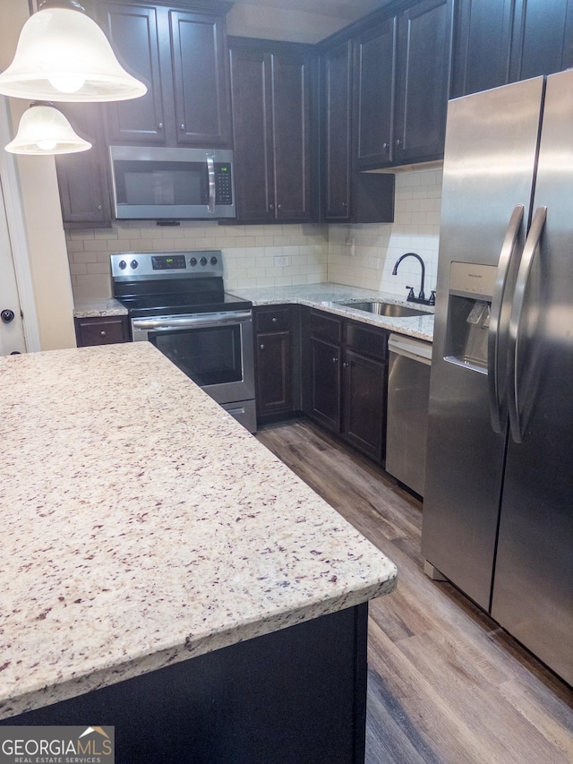 kitchen featuring hardwood / wood-style floors, stainless steel appliances, tasteful backsplash, sink, and hanging light fixtures