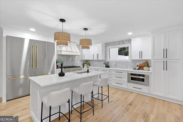 kitchen featuring a kitchen island with sink, backsplash, white cabinets, appliances with stainless steel finishes, and sink