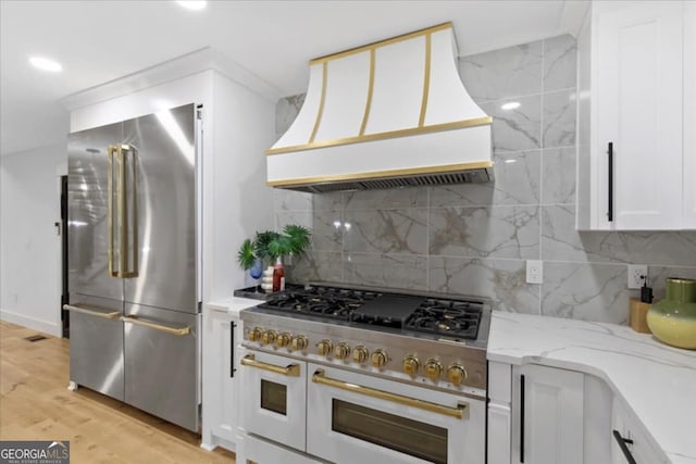 kitchen with premium range hood, high end appliances, tasteful backsplash, light wood-type flooring, and white cabinets