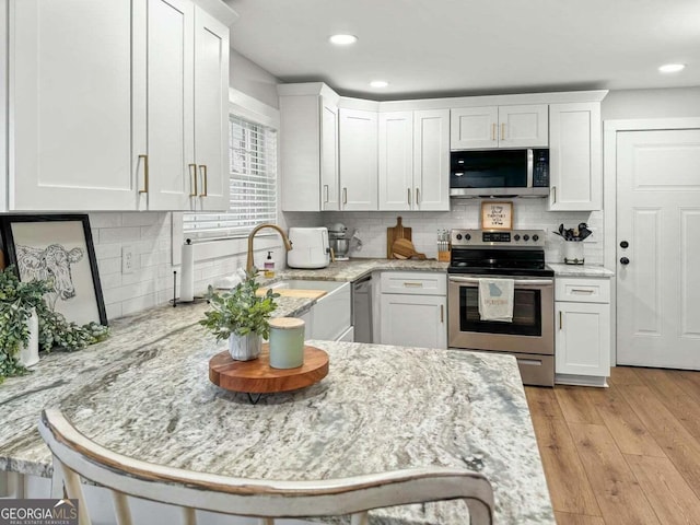 kitchen featuring light stone counters, stainless steel appliances, sink, white cabinetry, and a breakfast bar area