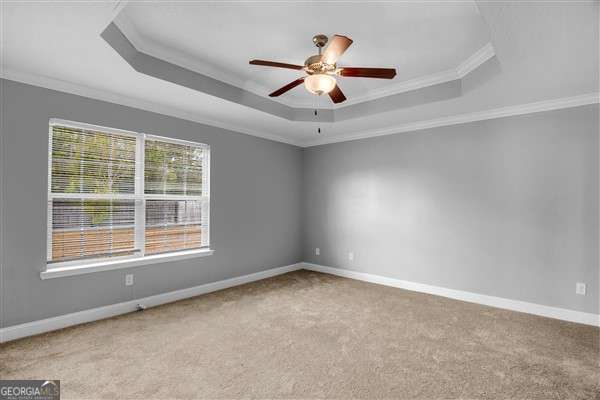 unfurnished room with ceiling fan, a raised ceiling, light colored carpet, and crown molding