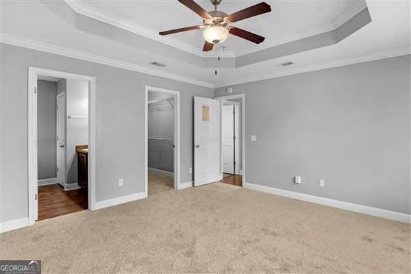 unfurnished bedroom featuring ceiling fan, a spacious closet, a tray ceiling, and ensuite bath