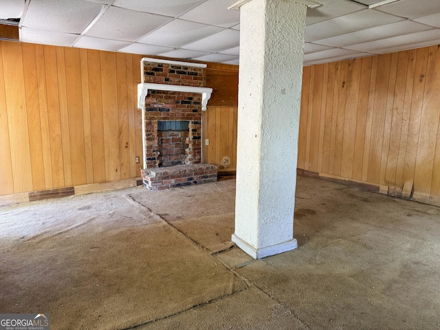 finished below grade area with a paneled ceiling, wood walls, and a brick fireplace