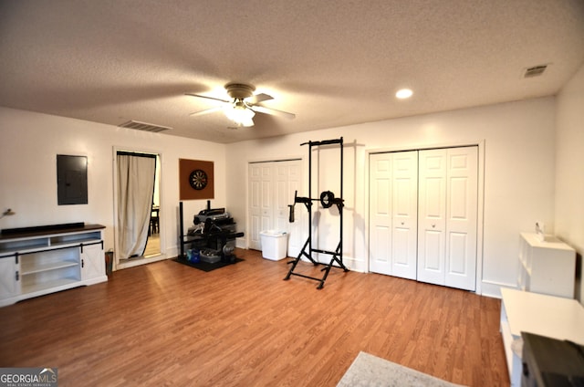 exercise room featuring hardwood / wood-style floors, ceiling fan, a textured ceiling, and electric panel