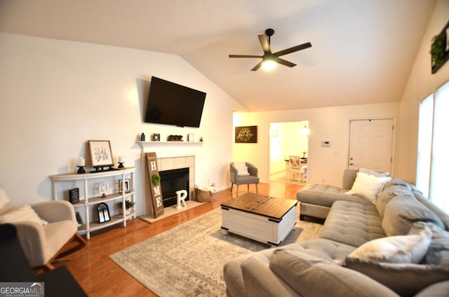 living room featuring hardwood / wood-style flooring, ceiling fan, lofted ceiling, and a tile fireplace