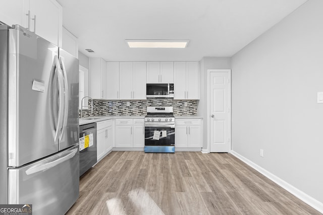 kitchen with white cabinetry, sink, stainless steel appliances, backsplash, and light hardwood / wood-style floors