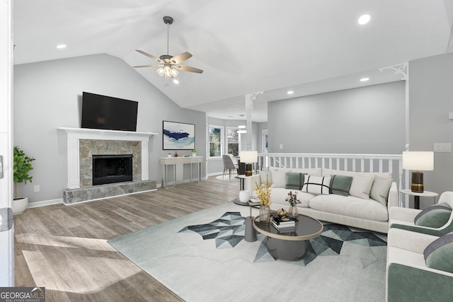 living room with a high end fireplace, wood-type flooring, vaulted ceiling, and ceiling fan