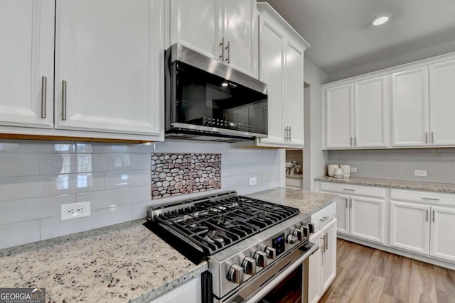 kitchen with white cabinets, appliances with stainless steel finishes, tasteful backsplash, and light stone counters