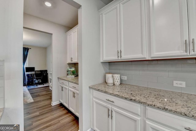 bar featuring white cabinets, light wood-type flooring, light stone countertops, and backsplash