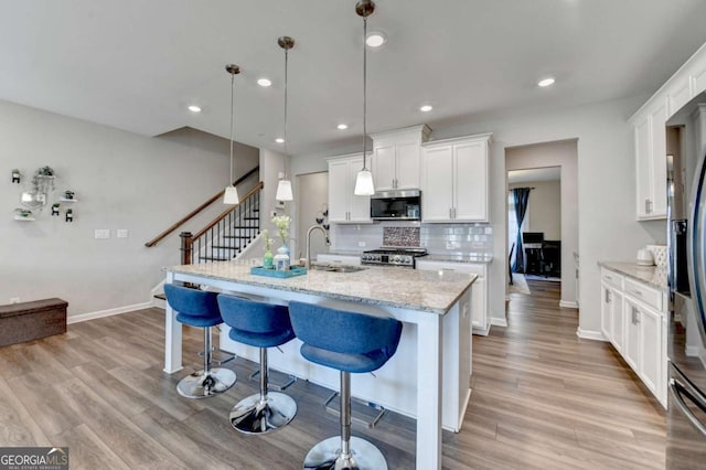 kitchen featuring hanging light fixtures, light stone counters, stove, a center island with sink, and white cabinets