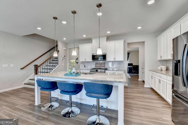 kitchen featuring pendant lighting, white cabinets, sink, an island with sink, and stainless steel appliances