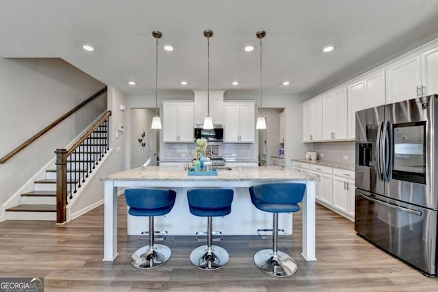 kitchen featuring white cabinets, decorative light fixtures, a kitchen island with sink, and appliances with stainless steel finishes