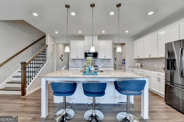 kitchen featuring stainless steel refrigerator with ice dispenser, white cabinetry, pendant lighting, and an island with sink