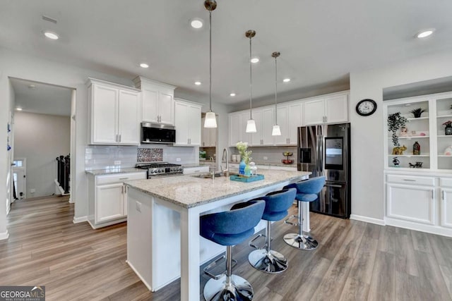 kitchen featuring pendant lighting, white cabinetry, an island with sink, and appliances with stainless steel finishes