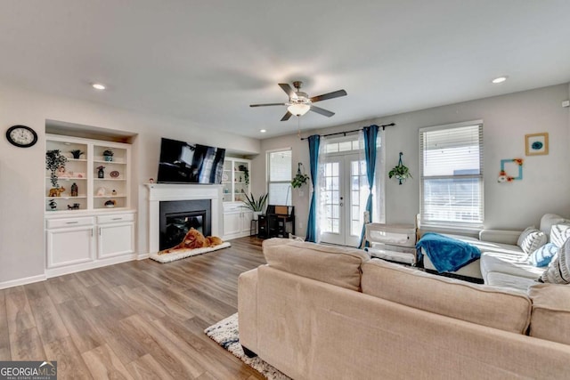 living room featuring built in shelves, ceiling fan, french doors, and hardwood / wood-style flooring