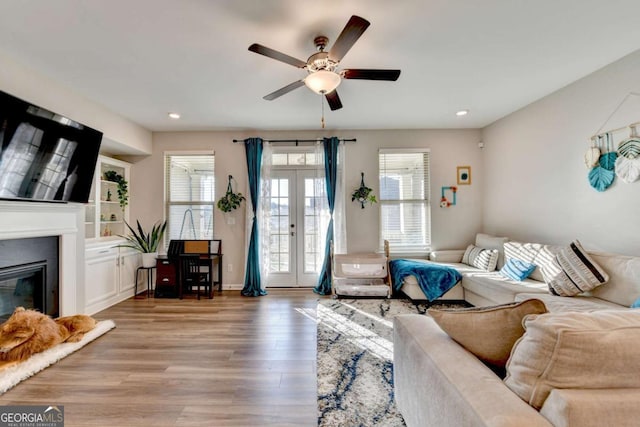 living room featuring hardwood / wood-style flooring, built in shelves, ceiling fan, and french doors