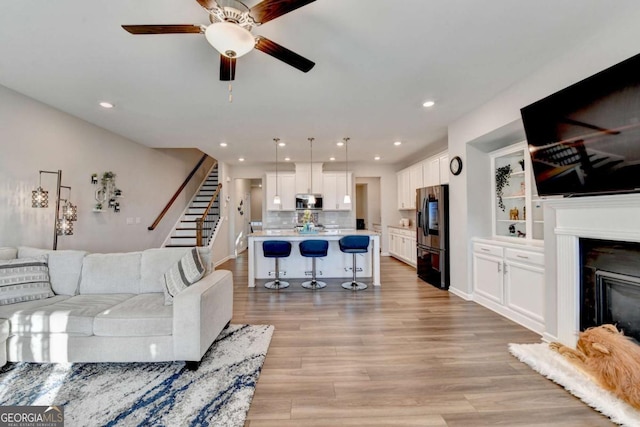 living room with built in shelves, light hardwood / wood-style flooring, and ceiling fan