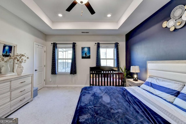 carpeted bedroom featuring multiple windows, a raised ceiling, and ceiling fan