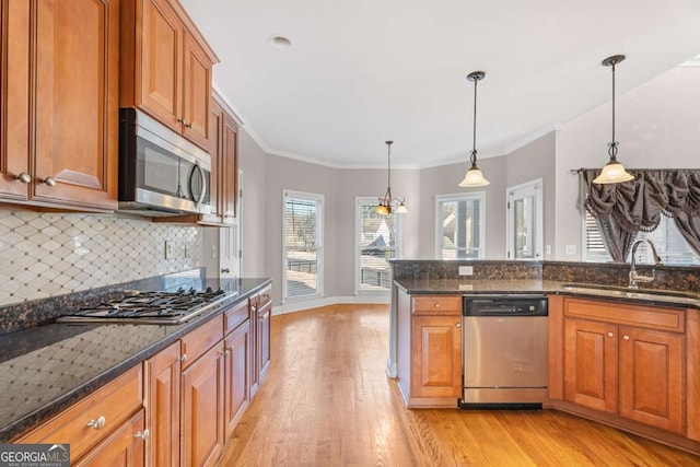 kitchen featuring crown molding, light hardwood / wood-style flooring, dark stone countertops, decorative light fixtures, and stainless steel appliances