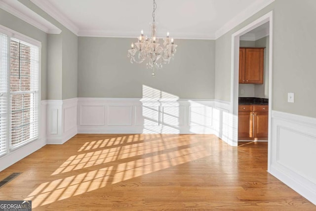 unfurnished dining area featuring crown molding, light wood-type flooring, and a notable chandelier