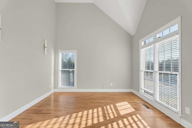 unfurnished room featuring plenty of natural light, high vaulted ceiling, and light hardwood / wood-style flooring