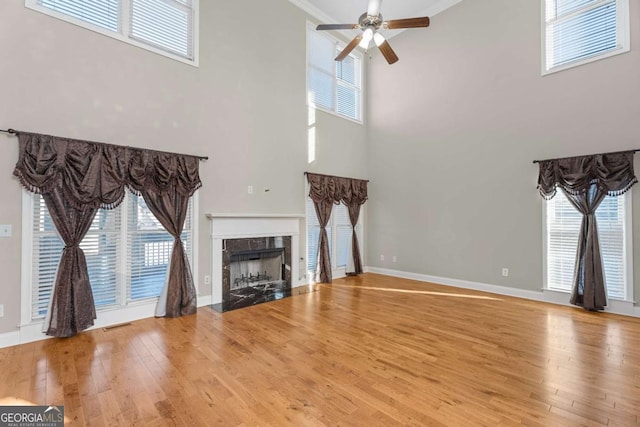 unfurnished living room with a fireplace, a high ceiling, hardwood / wood-style flooring, and ceiling fan