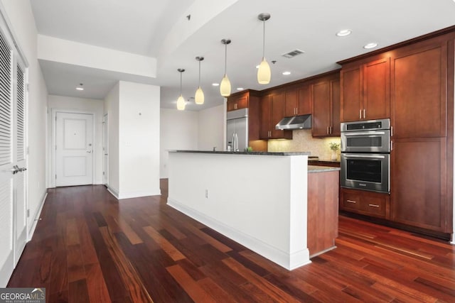 kitchen with a center island, dark wood-type flooring, hanging light fixtures, appliances with stainless steel finishes, and tasteful backsplash