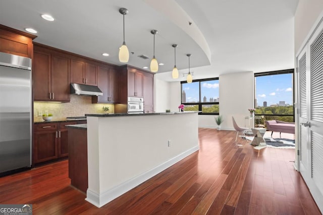 kitchen featuring hanging light fixtures, white oven, backsplash, built in refrigerator, and a kitchen island