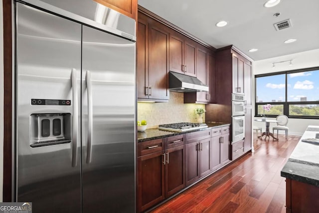 kitchen with decorative backsplash, stainless steel appliances, dark wood-type flooring, and dark stone countertops