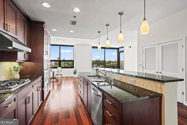 kitchen featuring appliances with stainless steel finishes, backsplash, dark stone counters, dark wood-type flooring, and pendant lighting