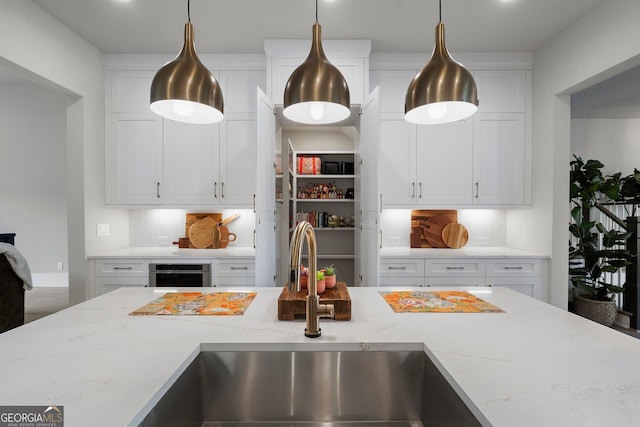 kitchen with light stone countertops, sink, white cabinetry, and pendant lighting