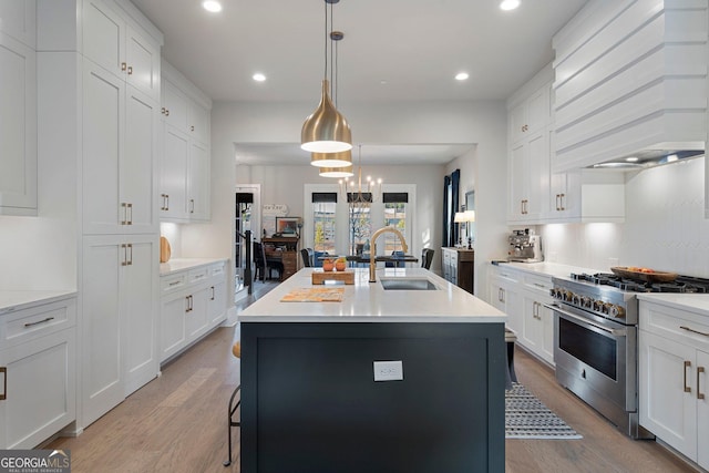 kitchen with sink, hanging light fixtures, stainless steel range, an island with sink, and custom range hood