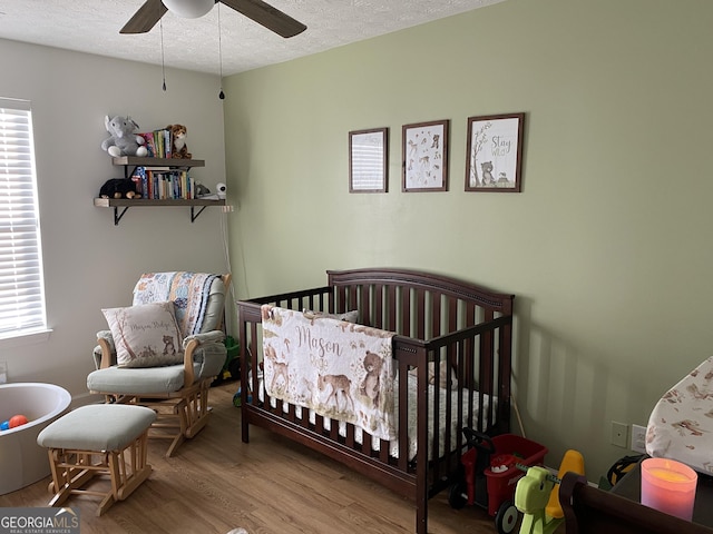 bedroom with multiple windows, ceiling fan, hardwood / wood-style floors, and a crib