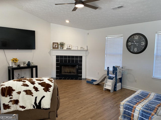 bedroom with hardwood / wood-style floors, a textured ceiling, ceiling fan, and a tiled fireplace