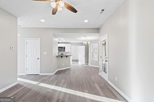 unfurnished living room featuring light wood-type flooring, ceiling fan with notable chandelier, and a textured ceiling