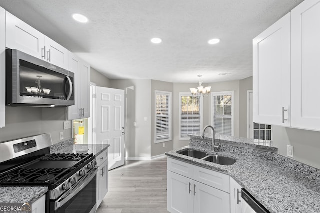 kitchen featuring stainless steel appliances, light stone countertops, a chandelier, white cabinets, and sink