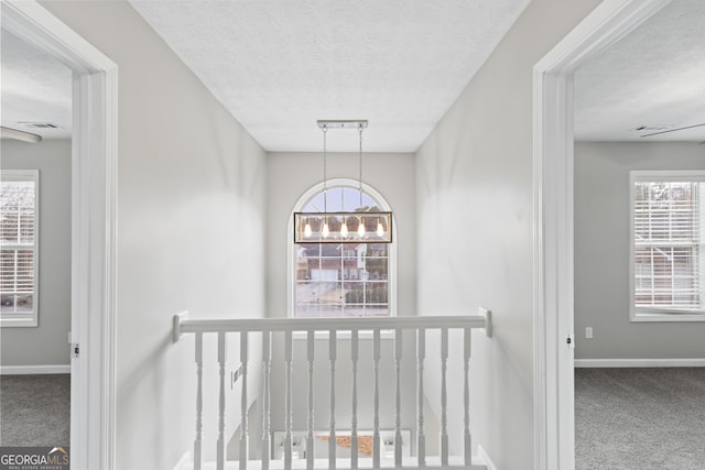 corridor featuring carpet, a chandelier, and a textured ceiling