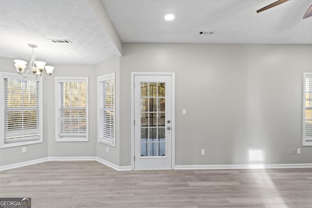 unfurnished room with ceiling fan with notable chandelier and light hardwood / wood-style flooring