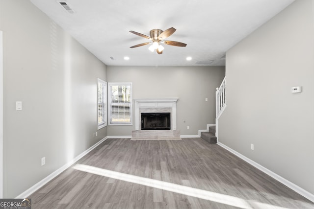 unfurnished living room with a premium fireplace, hardwood / wood-style flooring, and ceiling fan