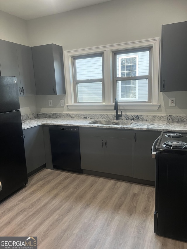 kitchen with gray cabinetry, black appliances, sink, light hardwood / wood-style flooring, and light stone countertops