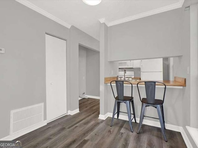 dining area with dark wood-type flooring, crown molding, and sink