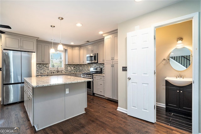 kitchen featuring a kitchen island, appliances with stainless steel finishes, sink, hanging light fixtures, and light stone counters