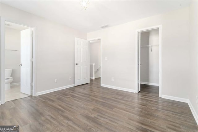 unfurnished bedroom featuring a spacious closet, ensuite bath, a closet, and dark wood-type flooring