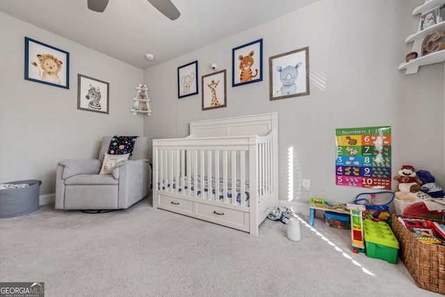 bedroom featuring a nursery area, ceiling fan, and carpet flooring