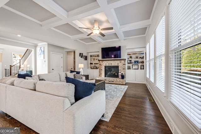 living room featuring dark hardwood / wood-style floors, a brick fireplace, built in features, ceiling fan, and beamed ceiling