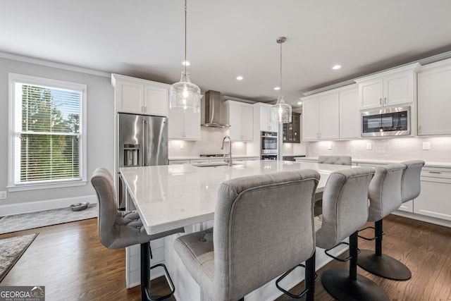 kitchen featuring a center island with sink, stainless steel appliances, pendant lighting, sink, and wall chimney range hood