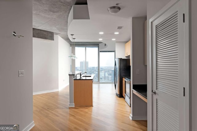 kitchen with stainless steel fridge, stove, pendant lighting, a wall of windows, and light hardwood / wood-style floors